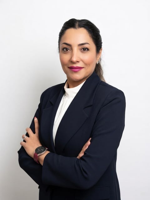 Professional headshot of a woman wearing a dark blazer and white shirt with arms crossed, smiling against a white background