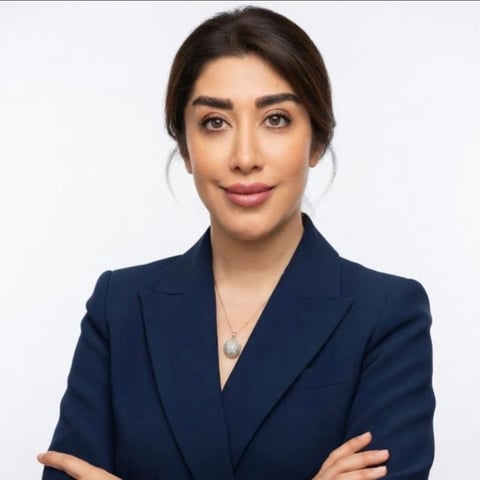 Professional headshot of a woman with dark hair wearing a dark blue blazer, arms crossed, against a white background